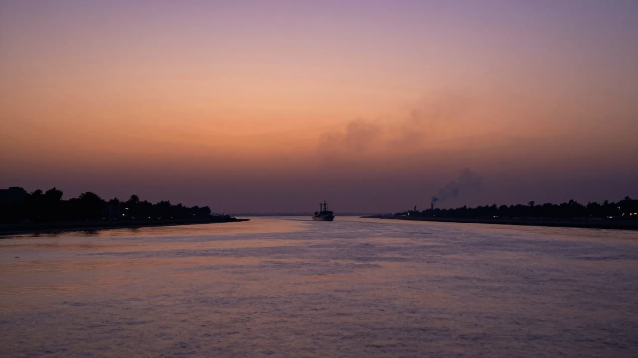 A realistic view of the Strait of Hormuz at dusk with distant military smoke and water reflections.