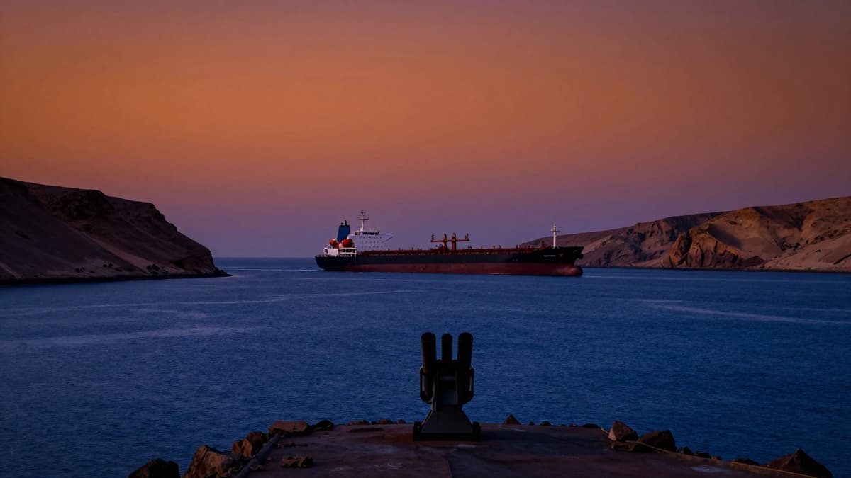 Silhouette of a naval launcher and oil tanker on the Strait of Hormuz at sunset.