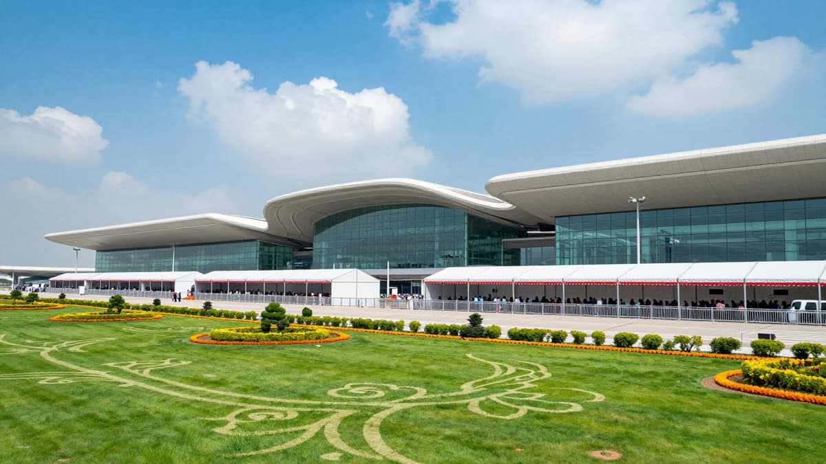 A modern international airport terminal with glass facades and event tents under a blue sky.