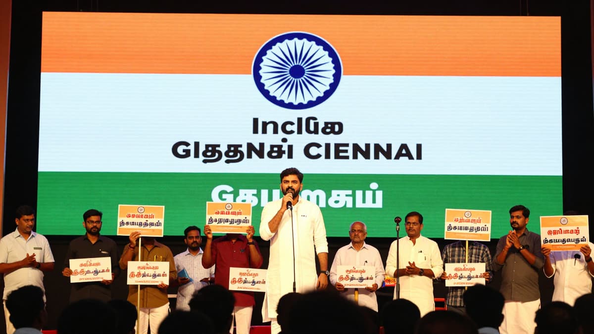 A crowded election rally stage in Tamil Nadu with national flags and microphones for a major political announcement.