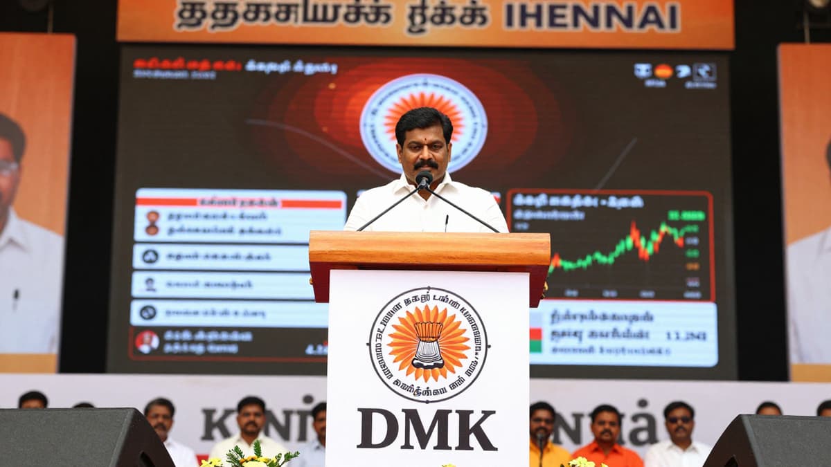 A political rally stage in Chennai displaying the DMK logo and Tamil Nadu flag under warm lighting.