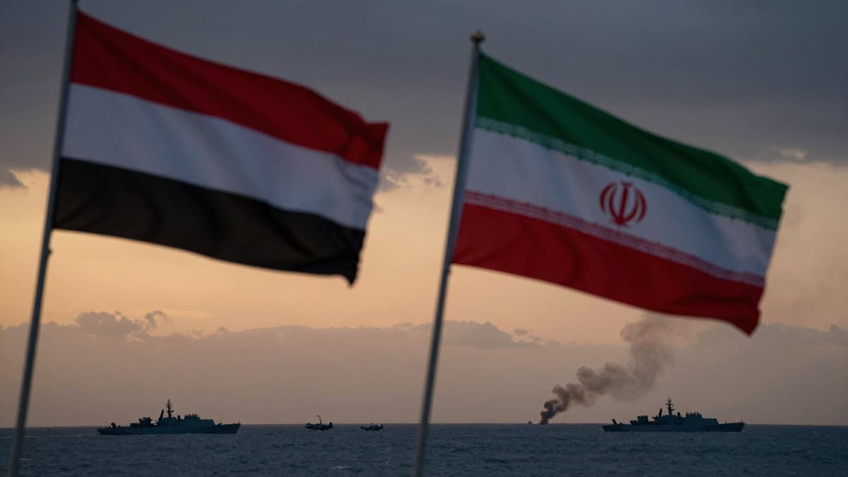 Flags of Iran and Yemen waving over the Middle East with distant smoke plumes indicating regional conflict and military activity.