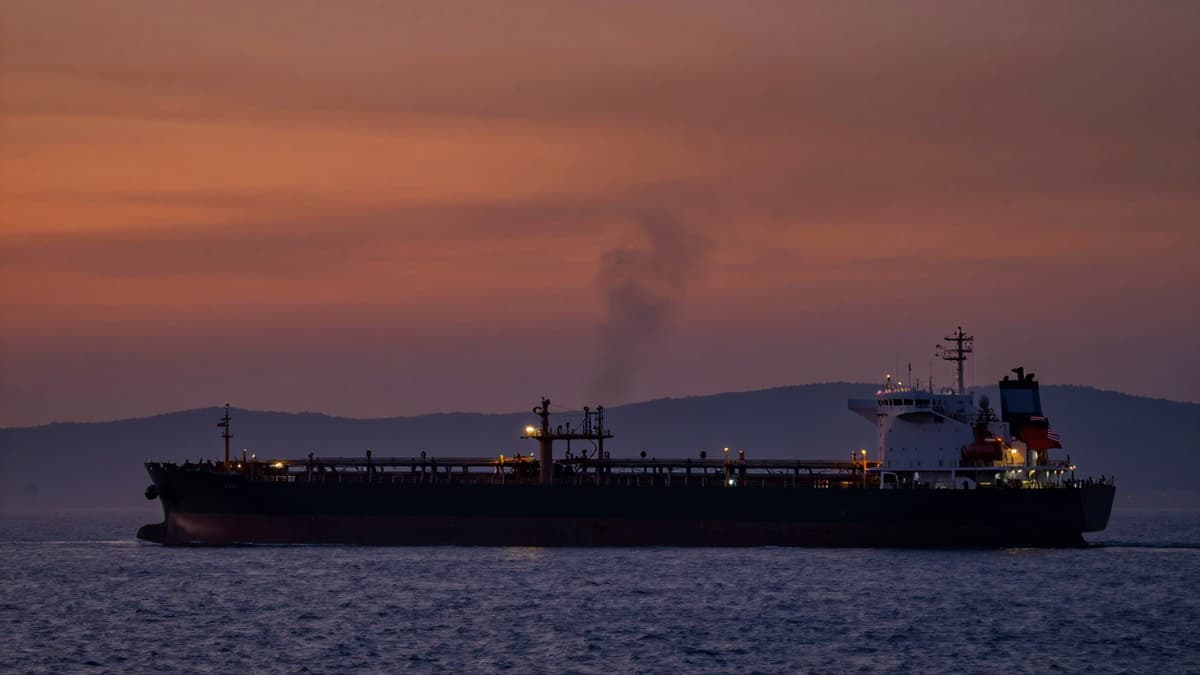 A realistic view of a tanker in the Strait of Hormuz under a smoky sky with flags of Iran and the US visible.