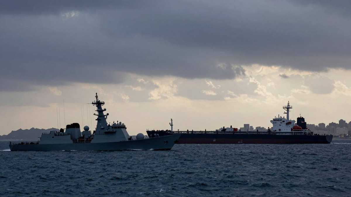 Warships and an oil tanker in the Persian Gulf under stormy skies, symbolizing the conflict over the vital waterway.