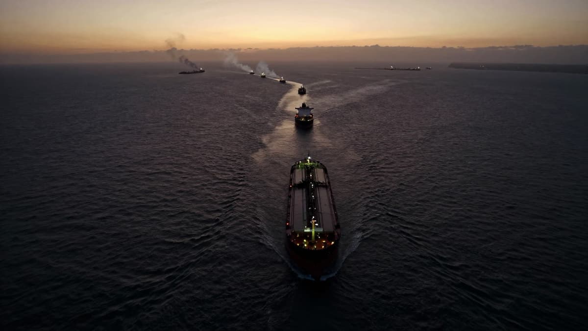 Realistic aerial view of a crowded shipping channel with oil tankers and distant smoke plumes representing a maritime crisis.