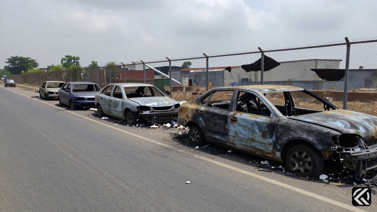Burnt vehicles and scattered debris on an industrial road in Noida following a protest.