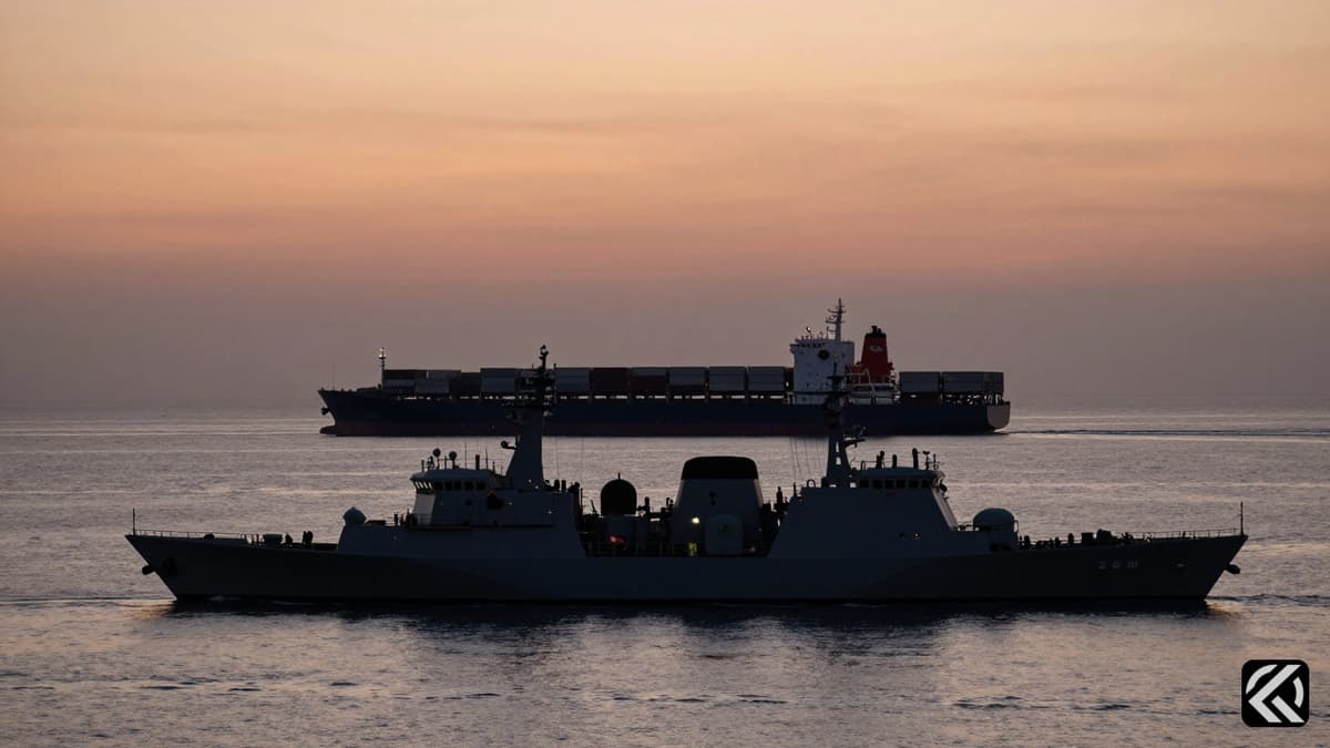 Silhouette of a military patrol boat and container ship near a narrow strait entrance at dusk.