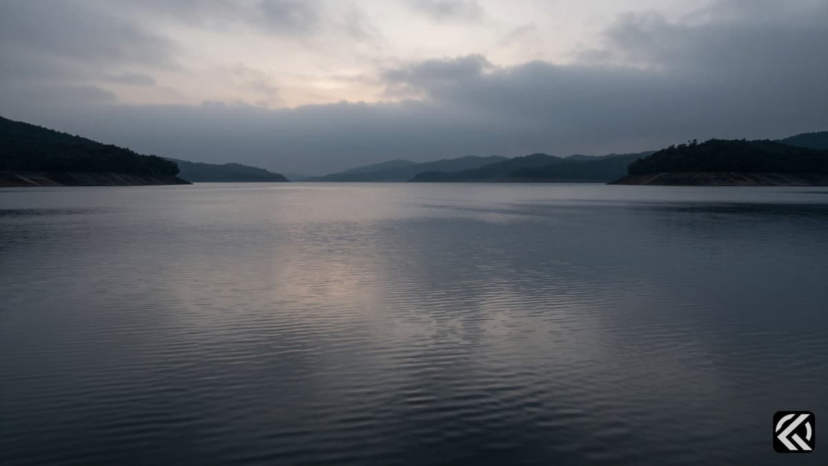Somber calm waters of a large dam reservoir under an overcast sky representing tragedy and recovery.