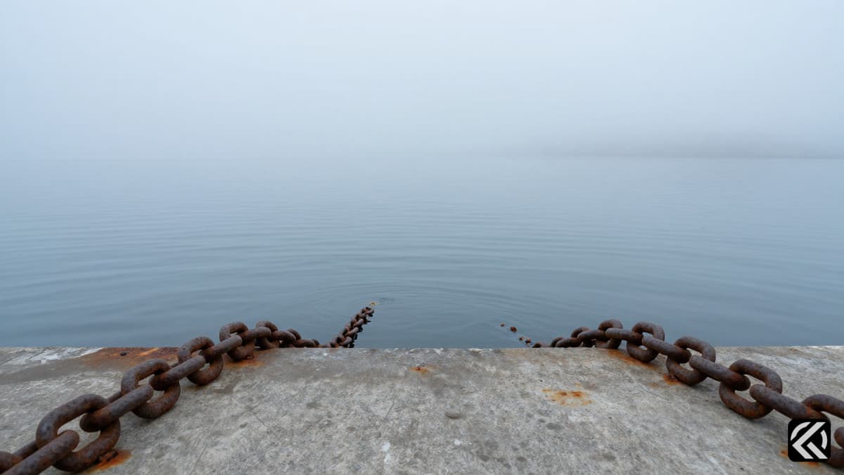 Heavy metal chains resting on a concrete dock beside calm, foggy maritime waters symbolizing a naval blockade.