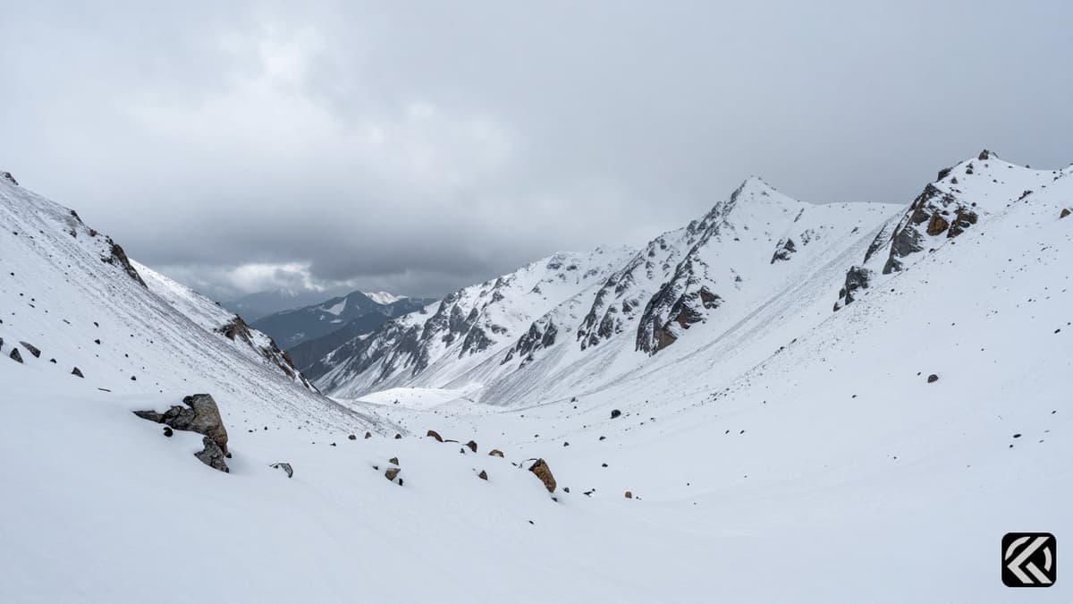 Snowy high-altitude mountain pass under cloudy skies representing difficult terrain for climbers.