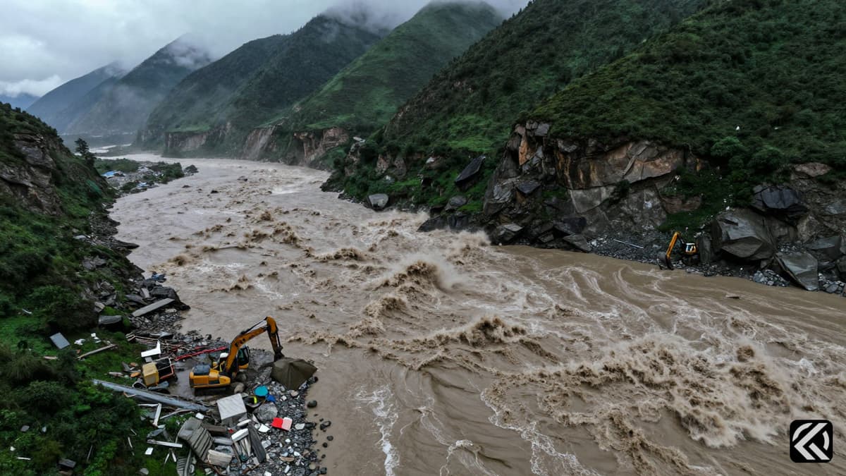 Muddy floodwaters surge through a mountain valley near a disaster site.